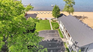 A hotel with a parking lot, a beach view, and a building with a balcony overlooking the beach. - Sandbar Cottage 4 Lakefront 1BR cottage with kitchen, patio, A/C, and parking. (Traverse City)