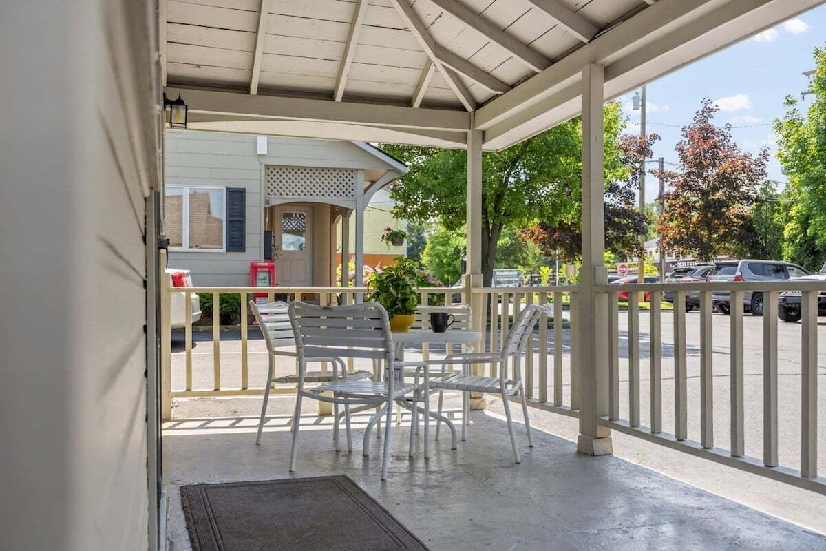 A covered outdoor seating area with metal chairs and a table, overlooking a parking lot and street.