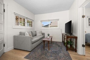 A compact living space with a grey sofa, a small wooden table, a television, and a patterned rug.