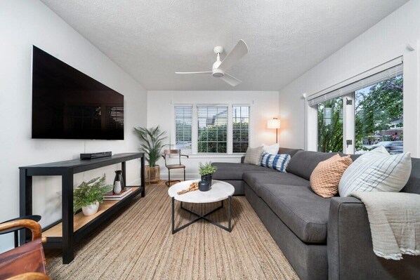 Un salon moderne avec un canapé gris, une table basse ronde, un meuble TV noir et un ventilateur de plafond.
