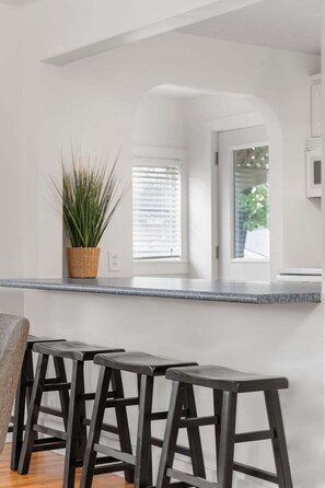 Une cuisine moderne avec un plan de travail blanc, une plante en pot et trois tabourets noirs.