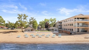 Un hotel fronte spiaggia con diversi edifici, una spiaggia sabbiosa con lettini e un cielo sereno.
