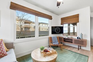 A living room with a sofa, a coffee table with snacks, a TV, and a window with a view of buildings.