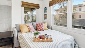 Ein Schlafzimmer mit Bett, Nachttisch, Fenster mit Jalousien und Blick nach draußen.