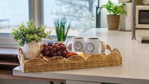 Eine Küchenarbeitsplatte mit einem Korbtablett, das Trauben, Käse und zwei Kaffeetassen mit dem Schriftzug 'Elevated' enthält.