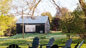 Ein rustikaler Schuppen mit einer Metallbedeckung, umgeben von einer grünen Wiese mit mehreren Adirondack-Stühlen.