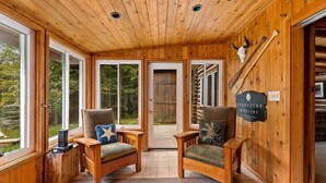 A cozy cabin interior with wooden walls, two armchairs with cushions, a wooden bench, and a sign indicating 'Fiddleton Midnight'. - Boardman River Cabin (Traverse City)