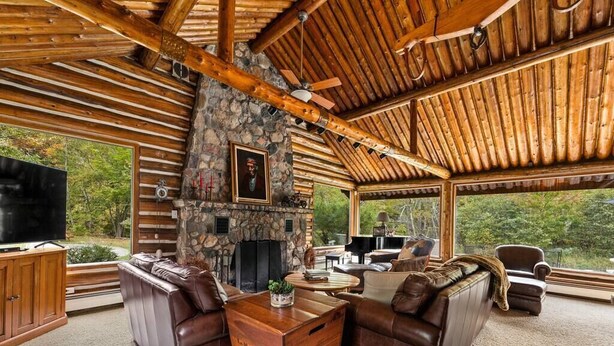 A log cabin interior with a stone fireplace, leather sofas, a wooden coffee table, and a television. - Boardman River Cabin (Traverse City)