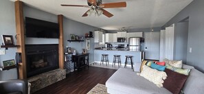 Ein modernes Wohnzimmer mit Kamin, Deckenventilator und einer Küchenzeile mit Barhocker.