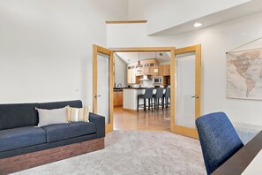A modern living room with a sofa, a coffee table, and a dining area with chairs and a kitchen in the background.