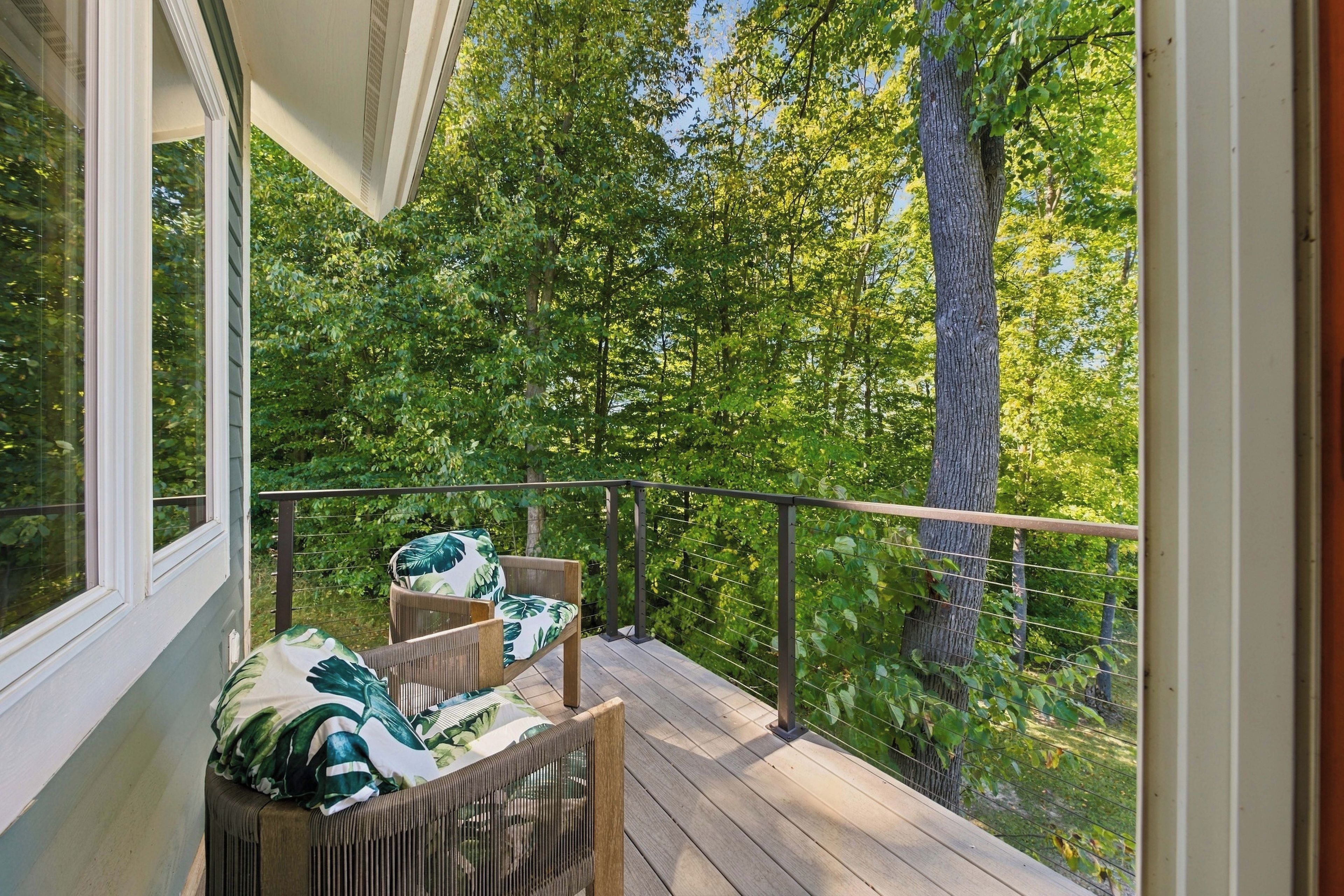A wooden deck with two wicker chairs and a table, overlooking a dense forest.