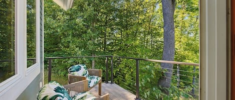 A wooden deck with two wicker chairs and a table, overlooking a dense forest.