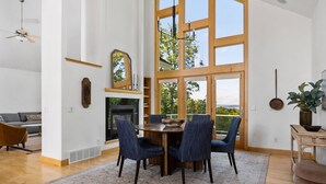 A dining area with a wooden table and chairs, a fireplace, and large windows offering a view of the outdoors. - Seven Hills Estate on Old Mission (Traverse City)