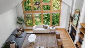 A spacious living room with a large window, a fireplace, and a ceiling fan. - Seven Hills Estate on Old Mission (Traverse City)