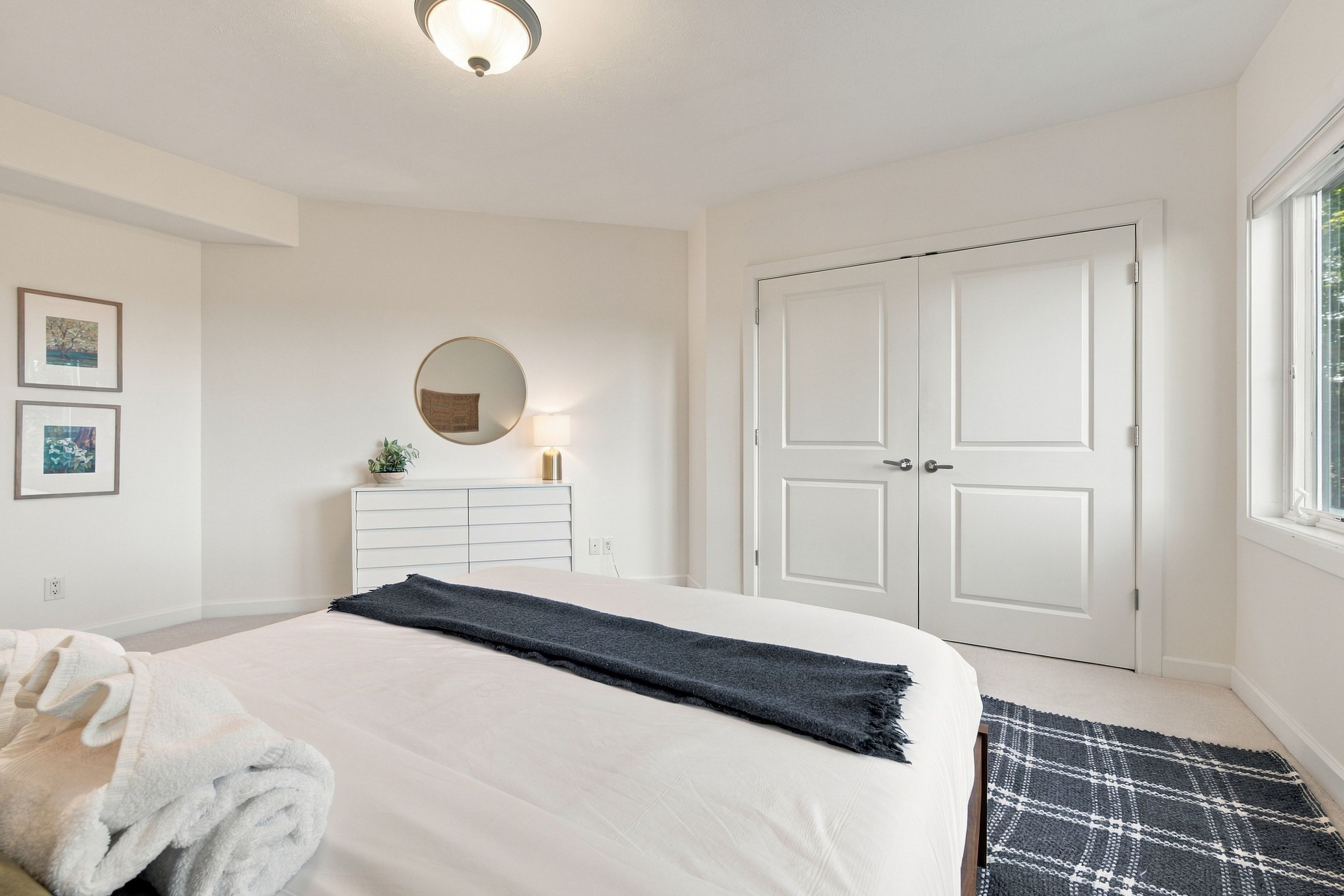 A bedroom with a bed, a dresser, a mirror, a door, and a window.