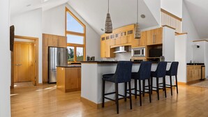 A modern kitchen with wooden cabinets, a stainless steel refrigerator, and a bar area with four stools. - Seven Hills Estate on Old Mission (Traverse City)