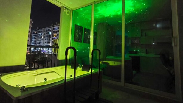 Et moderne hotelværelse med stort vindue, jacuzzi og udsigt over byen om natten.