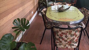 A sunroom with wooden walls, a round table, chairs, and potted plants.