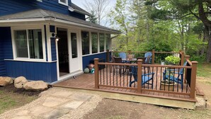 A covered deck with outdoor furniture, a wooden railing, and a house with blue siding and white trim.
