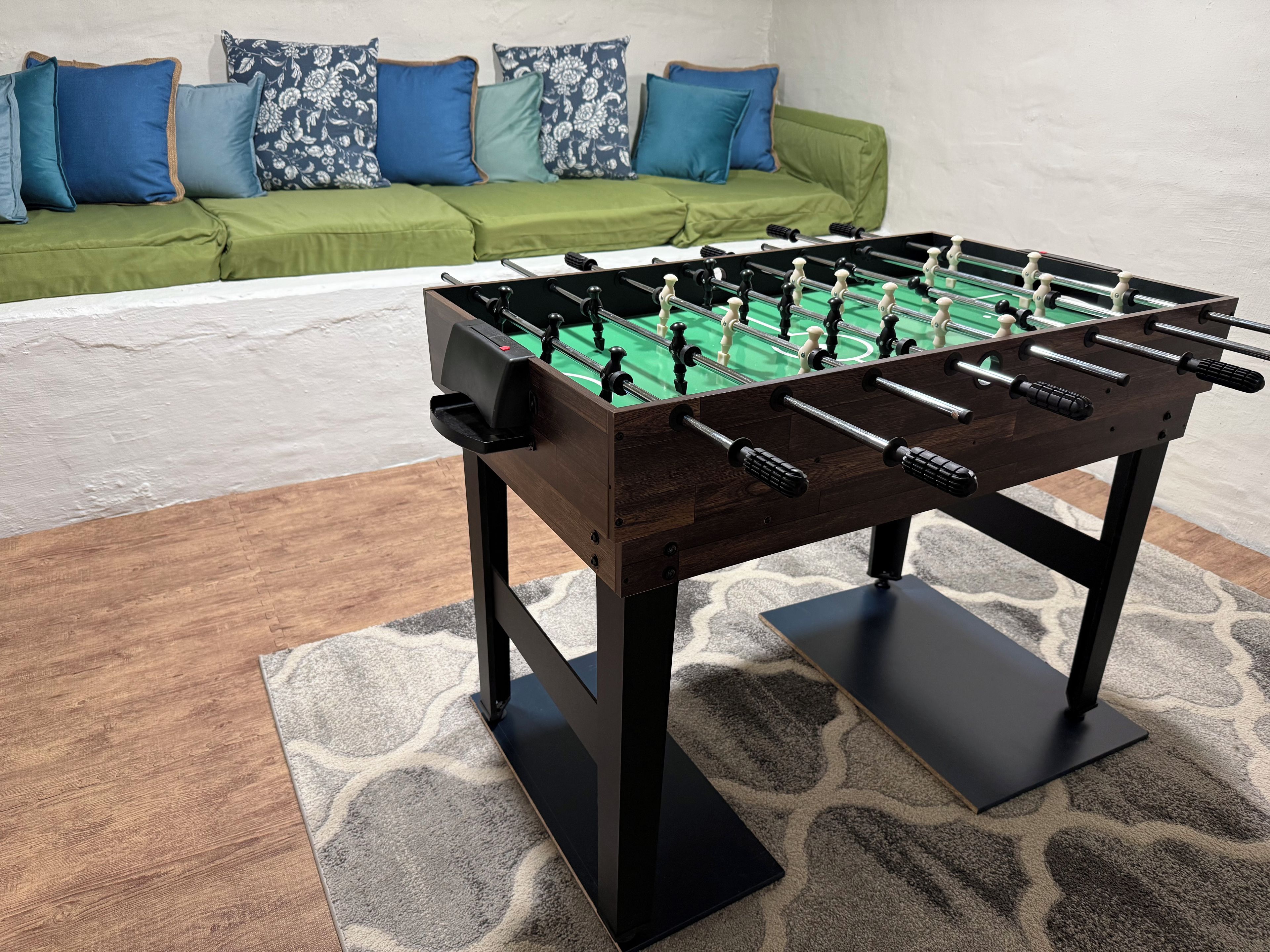 A foosball table in a room with a green sofa and patterned cushions.