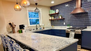 A kitchen with a large island, dark blue cabinets, a stainless steel stove, and pendant lighting.