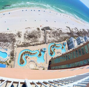 A beach resort with a large pool area, a sandy beach, and a view of the ocean. - NEW Phoenix Gulf Tower II Unit 2508 | Luxury East Corner - Gorgeous Coastal Decor, Stunning Views (Orange Beach)