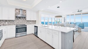 A modern kitchen with white cabinetry, a large island, and a view of the ocean. - NEW Phoenix Gulf Tower II Unit 2508 | Luxury East Corner - Gorgeous Coastal Decor, Stunning Views (Orange Beach)