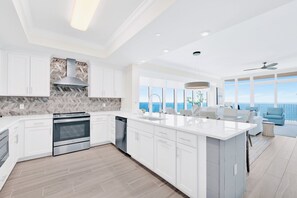 A modern kitchen with white cabinetry, a large island, and a view of the ocean. - NEW Phoenix Gulf Tower II Unit 2508 | Luxury East Corner - Gorgeous Coastal Decor, Stunning Views (Orange Beach)
