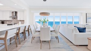 A modern kitchen with white cabinetry, a central island, and a view of the ocean through large windows. - NEW Phoenix Gulf Tower II Unit 2508 | Luxury East Corner - Gorgeous Coastal Decor, Stunning Views (Orange Beach)