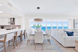 A modern kitchen with white cabinetry, a central island, and a view of the ocean through large windows. - NEW Phoenix Gulf Tower II Unit 2508 | Luxury East Corner - Gorgeous Coastal Decor, Stunning Views (Orange Beach)