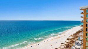 A beach with a clear view of the ocean, a sandy shore, and a building with multiple balconies. - NEW Phoenix Gulf Tower II Unit 2508 | Luxury East Corner - Gorgeous Coastal Decor, Stunning Views (Orange Beach)