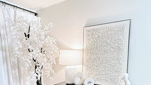 A modern room with a black cabinet, a potted white tree, a large abstract painting, and a white curtain. - The Cozy Abode On Beagle Street- 3BR 2BA -Sleeps 16- Pool (San Diego)