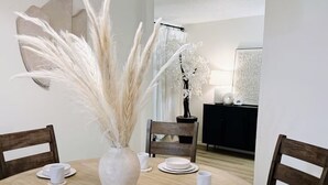 A dining area with a round table set for six, surrounded by wooden chairs. A large vase with pampas grass is placed in the center. - The Cozy Abode On Beagle Street- 3BR 2BA -Sleeps 16- Pool (San Diego)