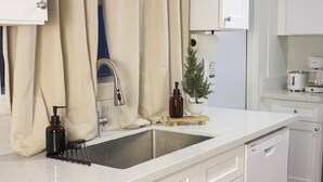 A modern kitchen with a white countertop, a stainless steel sink, a small potted plant, and a coffee maker. - The Cozy Abode On Beagle Street- 3BR 2BA -Sleeps 16- Pool (San Diego)