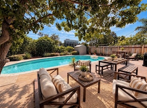 A poolside area with a wooden deck, lounge chairs, and a dining table. - The Cozy Abode On Beagle Street- 3BR 2BA -Sleeps 16- Pool (San Diego)