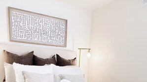 A neatly made bed with white linens, a decorative wall piece above, and a bedside lamp. - The Cozy Abode On Beagle Street- 3BR 2BA -Sleeps 16- Pool (San Diego)