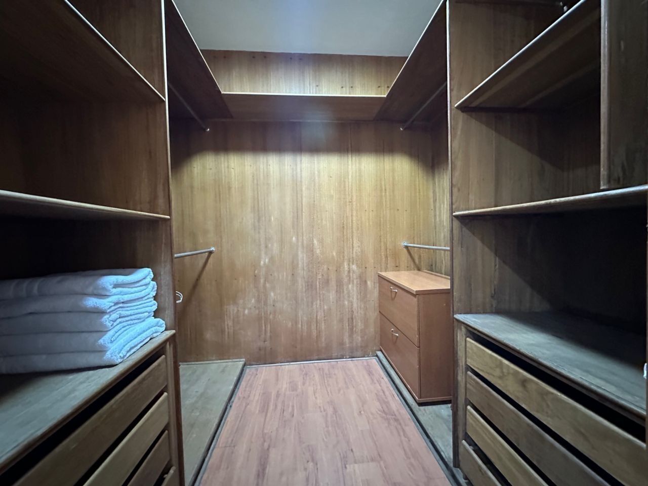 Un armario vestidor con estantes y cajones de madera, un pequeño mueble de madera y un techo inclinado.