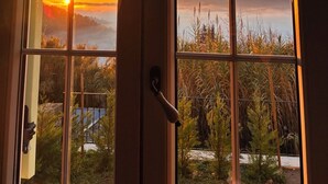 Blick durch ein Fenster auf einen Sonnenuntergang über einer Berg- und Vegetationslandschaft.