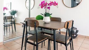 En matplats med ett träbord, fyra stolar, en vas med blommor, en spegel och en taklampa.