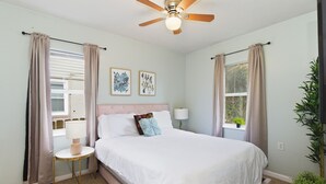A bedroom with a bed, a ceiling fan, a window with curtains, a bedside table with a lamp, and two wall art pieces. - 2 Bedroom Near Beltline, Mercedes Benz Stadium & State Farm Arena (Atlanta)