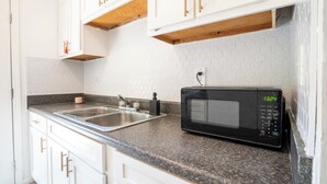 A kitchen with white cabinets, a granite countertop, a black microwave, and a double sink. - 2 Bedroom Near Beltline, Mercedes Benz Stadium & State Farm Arena (Atlanta)
