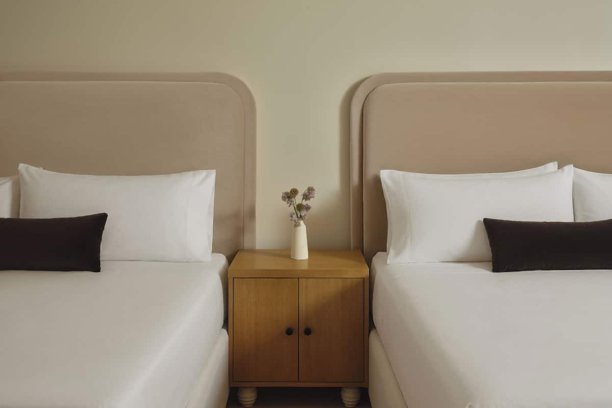 Une chambre d’hôtel avec deux lits, une table de chevet en bois et un vase rempli de fleurs.