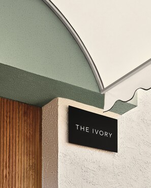 A sign with the text 'THE IVORY' mounted on a wall with a textured surface and a wooden panel. - The Ivory (Los Angeles)