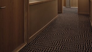 Un pasillo de hotel con puertas de madera, alfombra a cuadros y lámparas fijadas a la pared.