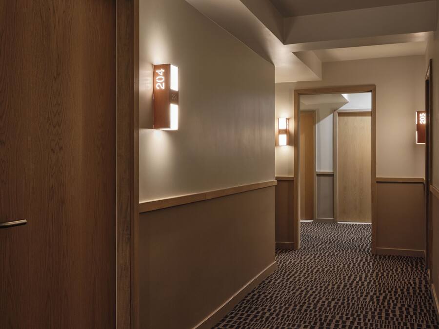 Ein Hotelgang mit Holztüren, einem Schachbrettmuster-Teppich und Wandleuchten.