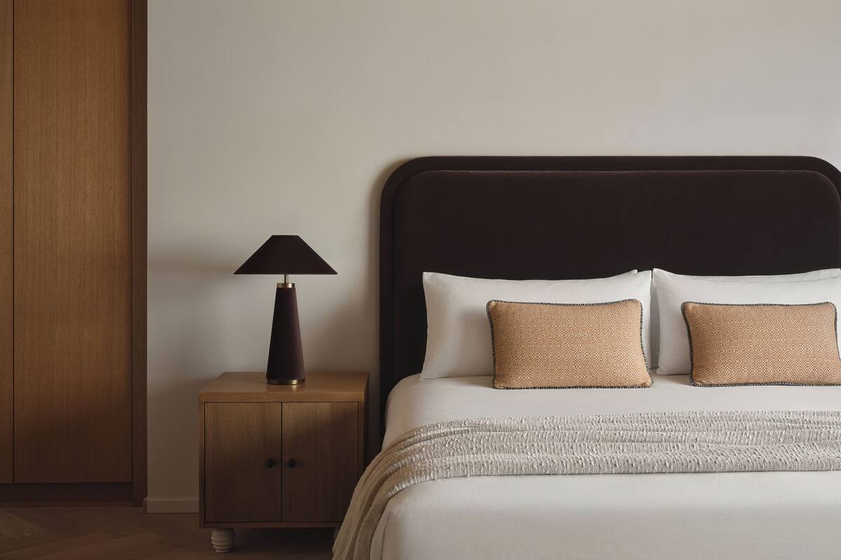 Un lit bien fait, avec une tête de lit sombre, une lampe de chevet et deux coussins à texture intéressante.
