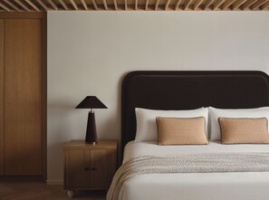 A neatly made bed with a dark headboard, a bedside lamp, and two textured pillows. - The Ivory (Los Angeles)