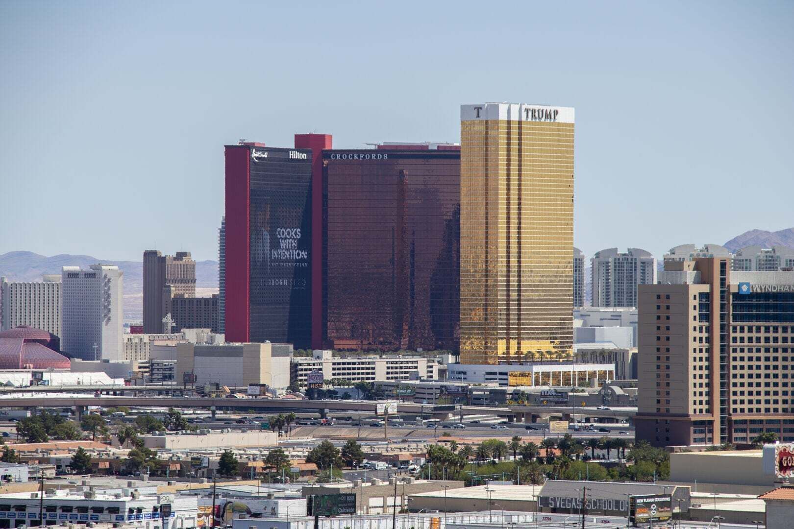 A cityscape with prominent buildings including a hotel with a 'Trump' sign, a 'Hilton' building, and a 'Crockfords' building.