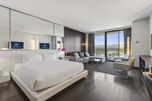 A modern hotel room with a large bed, a sofa, a coffee table, and a desk. There is a large window offering a view of the city. - SVS: 2BD/2.5BA Combo Suite | Strip & Mountain Views | Palms Place (Las Vegas)