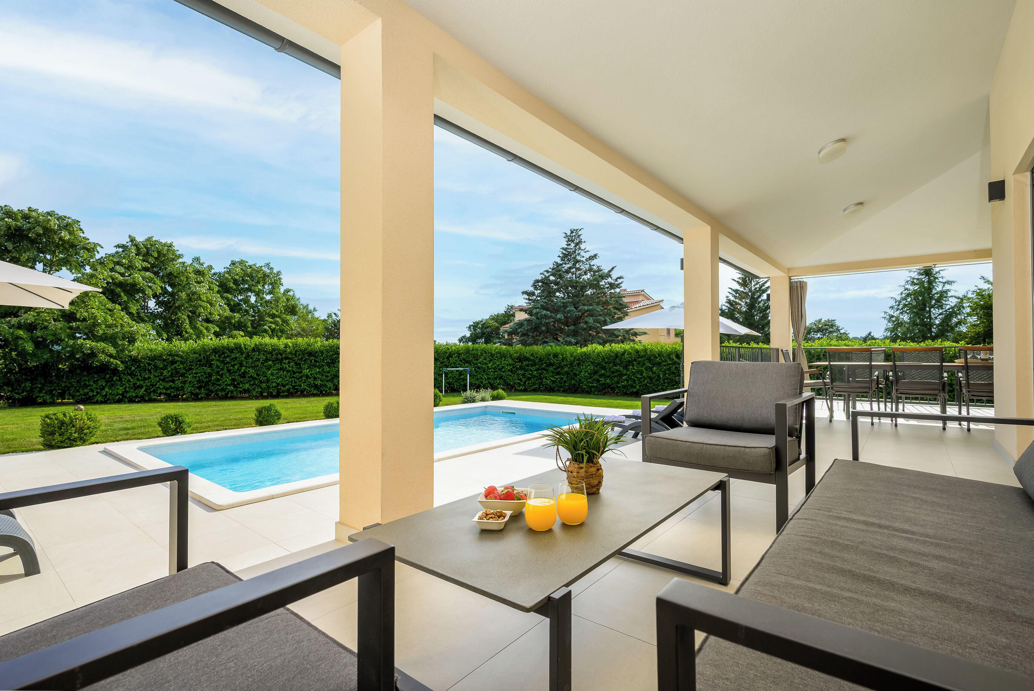 A covered outdoor area with a pool, seating, and a view of the surrounding greenery.